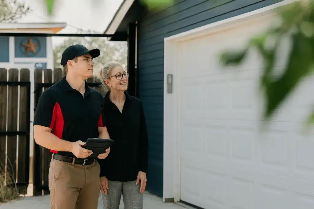 Garage door technician showing homeowner repair options outside a white residential garage.