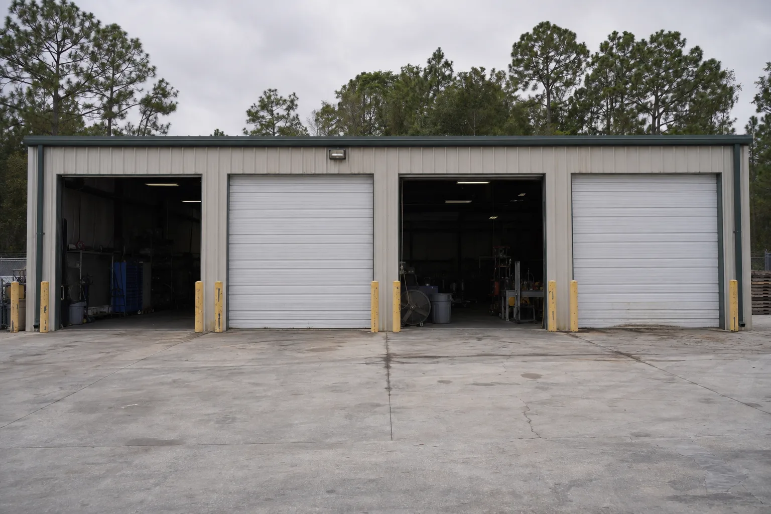 Four commercial sectional steel garage doors on the exterior of a low-rise service building, two open and two closed, with a concrete apron in the foreground and Florida pines under a bright sky
