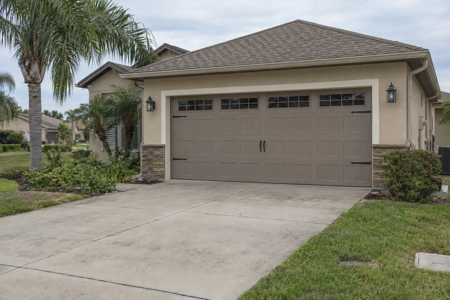 Carriage-style garage door in a taupe finish on a well-maintained single-story home in a Florida planned community, with a manicured lawn and matching neighbourhood streetscape behind it