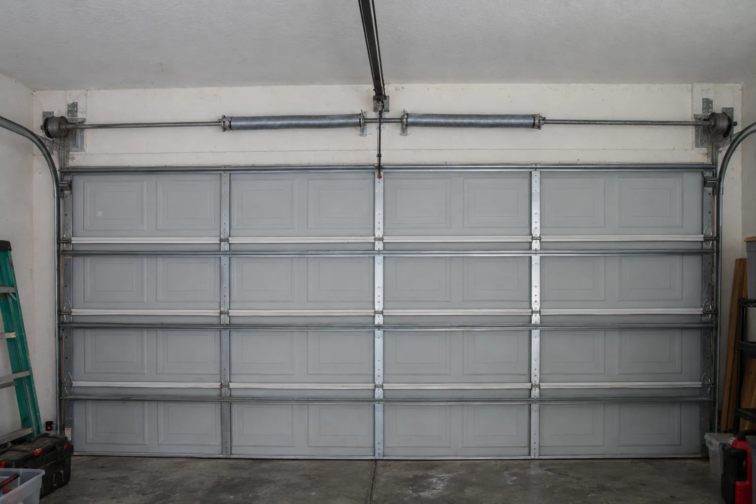 Pair of new galvanized torsion springs installed on the torsion bar above a closed residential garage door inside a Florida home, with winding cones and cable drums visible at each end