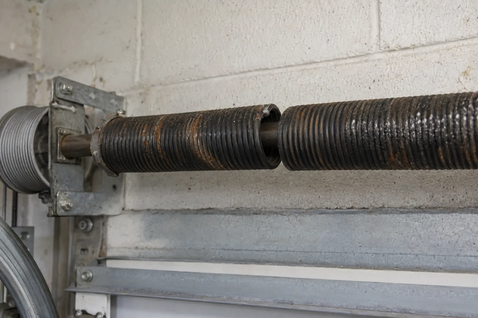 Close-up of a broken torsion spring on a steel torsion bar, showing a clear gap in the coil where the spring has snapped, with rust visible along the metal surface