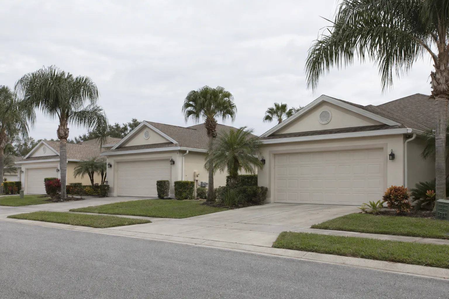 Row of single-story Florida ranch homes in a planned HOA community, each with matching white raised-panel garage doors, palm trees and manicured lawns in bright Orlando daylight
